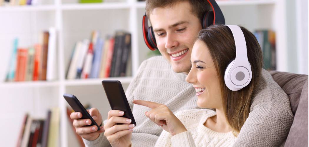 A couple sitting on sofa and listening music with headphones and hold phones